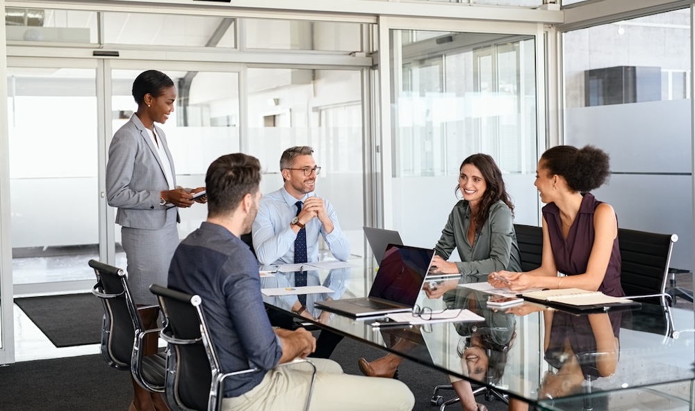 Smiling business team discussing work in meeting using laptop and documents in conference room. Successful business woman and businessmen discussing marketing strategy and ideas at meeting room. Corporate business man and woman with manager and secretary working together.